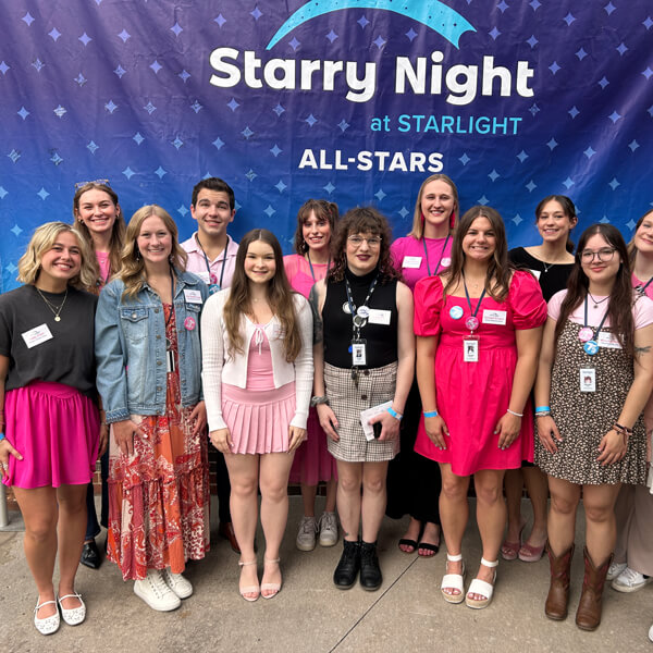 A group of young people stand together in front of a sign that says Starry Night at Starlight.