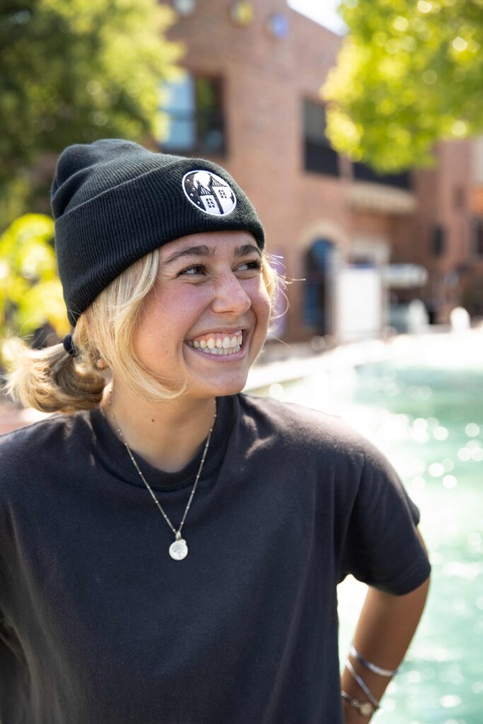 Woman wearing the Starlight beanie while laughing. The photo is taken in front of the fountain in the venue.