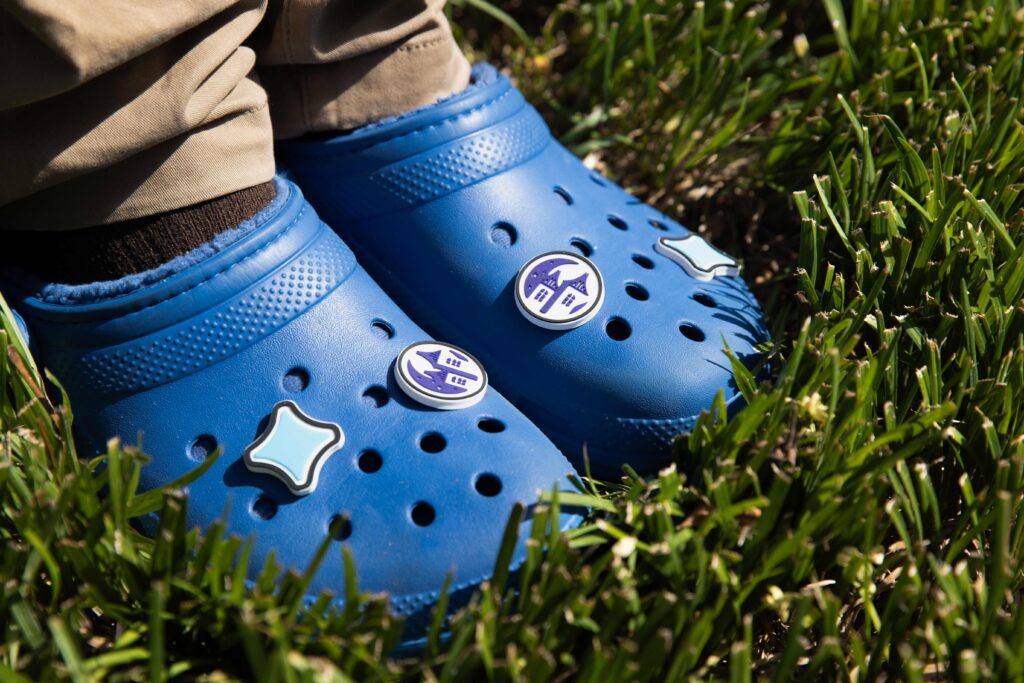 Two dark blue Crocs with 2 two different croc jibbitz on them. One is a light blue Starlight Star with black outline. The other is a dark blue Starlight Towers logo. The crocs are being worn in grass