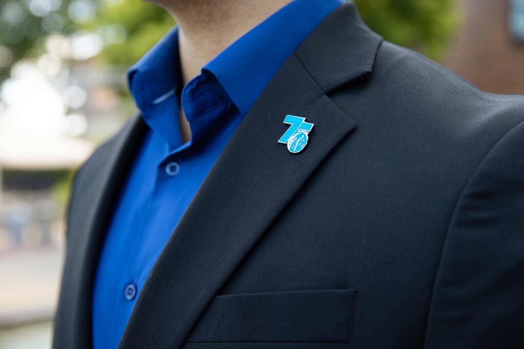 A 75th Starlight pin on a navy suit jacket. Man is standing with a blue shirt underneath with the venue in the background