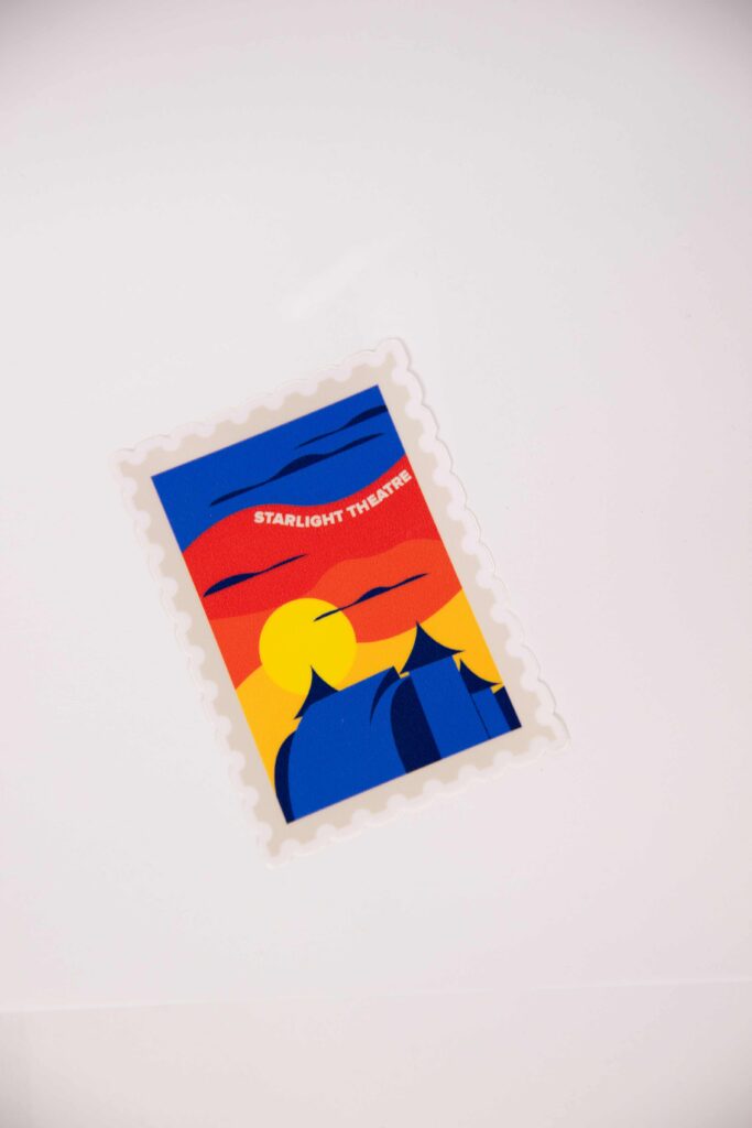 A starlight sticker with stamp like edges. The sticker has an animated Starlight stage house with a colorful sunset in the back. The text "starlight theater" can be seen in the sky by the clouds.