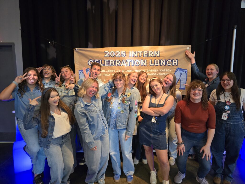 Group of all the interns standing in front of the jean party banner. They are doing their best silly faces.