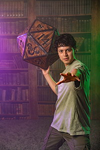Person posing with a giant 20-sided die in front of bookshelves.
