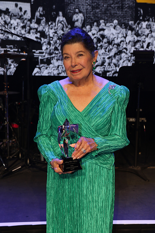 A woman in a green formal dress holds an award.