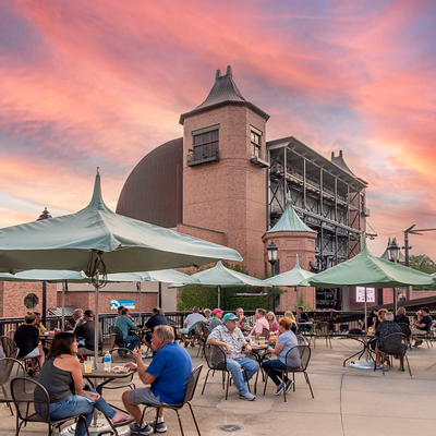 People eating and sitting on a deck with tables and umbrellas during sunset.
