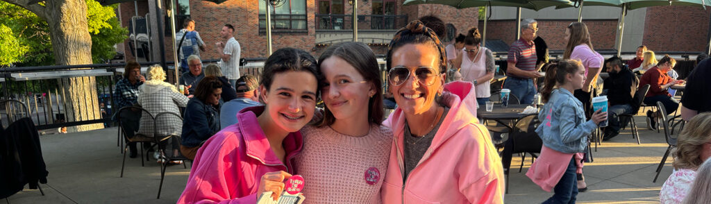 A woman and two younger girls dressed in pink smile and pose during a theme night event for Mean Girls.