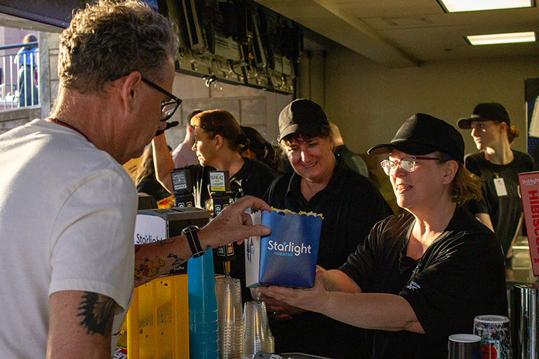 Concession worker hands a man a box of popcorn.
