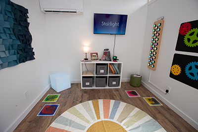Inside the Sensory Room with a rug, textured figure on the wall, books, and other activities.