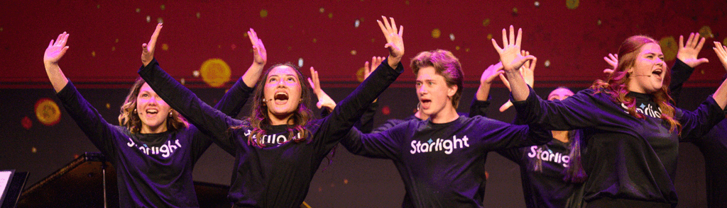 Students dressed in black shirts sing with their arms raised at Starlight's Gala.
