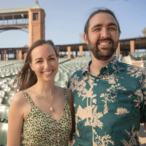 A white woman with long brown hair wearing a patterned dress and white male with a green patterned shirt