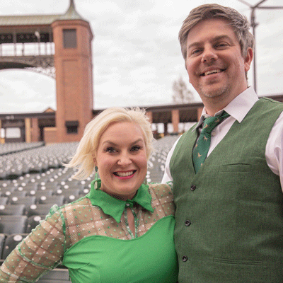 White woman with blonde hair wearing a green dress and a white male wearing a green vest and tie