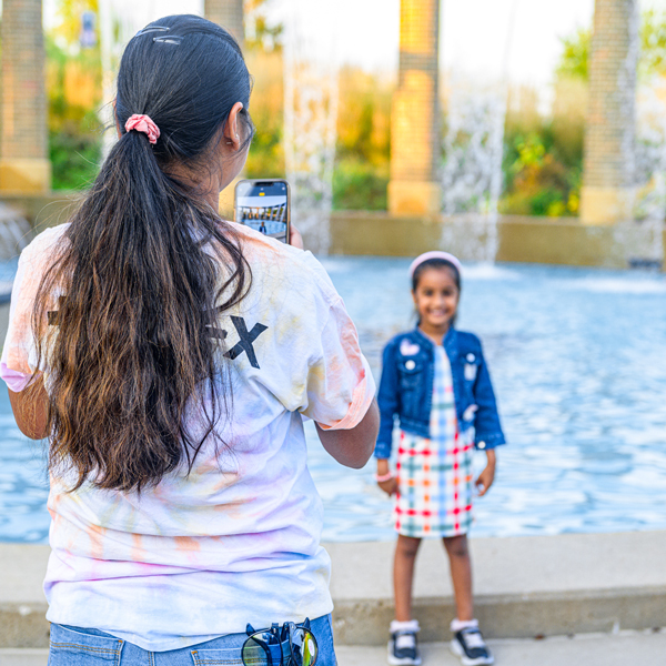 A young girl poses in front of the Starlight fountain while a woman takes her picture